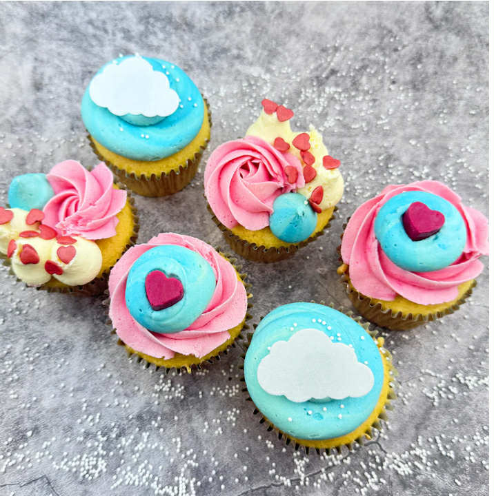 Each cupcake is baked fresh, swirled with dreamy pale pink and blue vanilla buttercream, topped with hearts and white sprinkles, and a handmade mini chocolate heart.